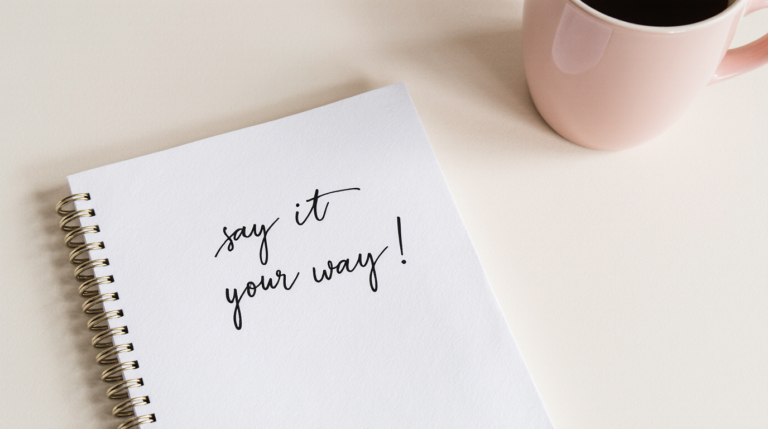 Spiral notebook with the handwritten phrase "Say It Your Way" beside a cup of coffee on a clean desk, symbolizing journaling and self-expression.