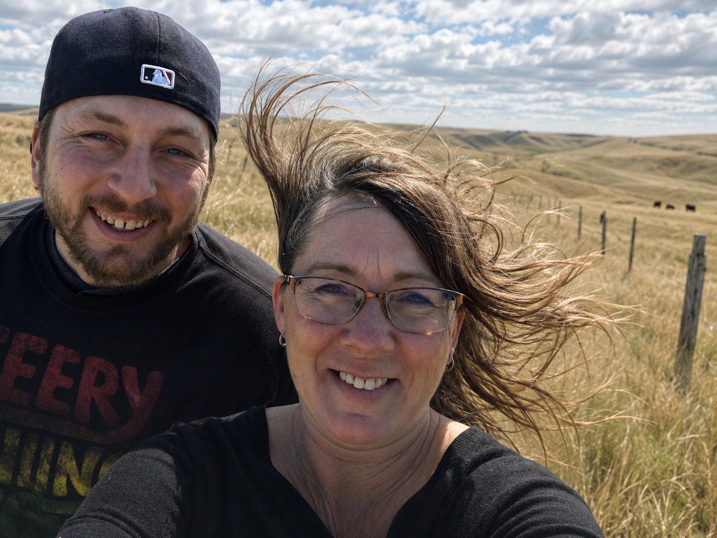Cleo and her son smiling in a wind-swept South Dakota pasture as strong prairie winds whip their hair during a ranch outing.